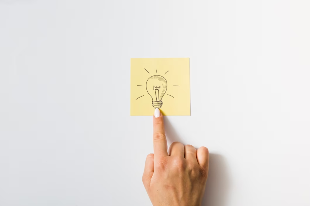 Hand with Yellow Sticky Note Featuring Light Bulb Drawing