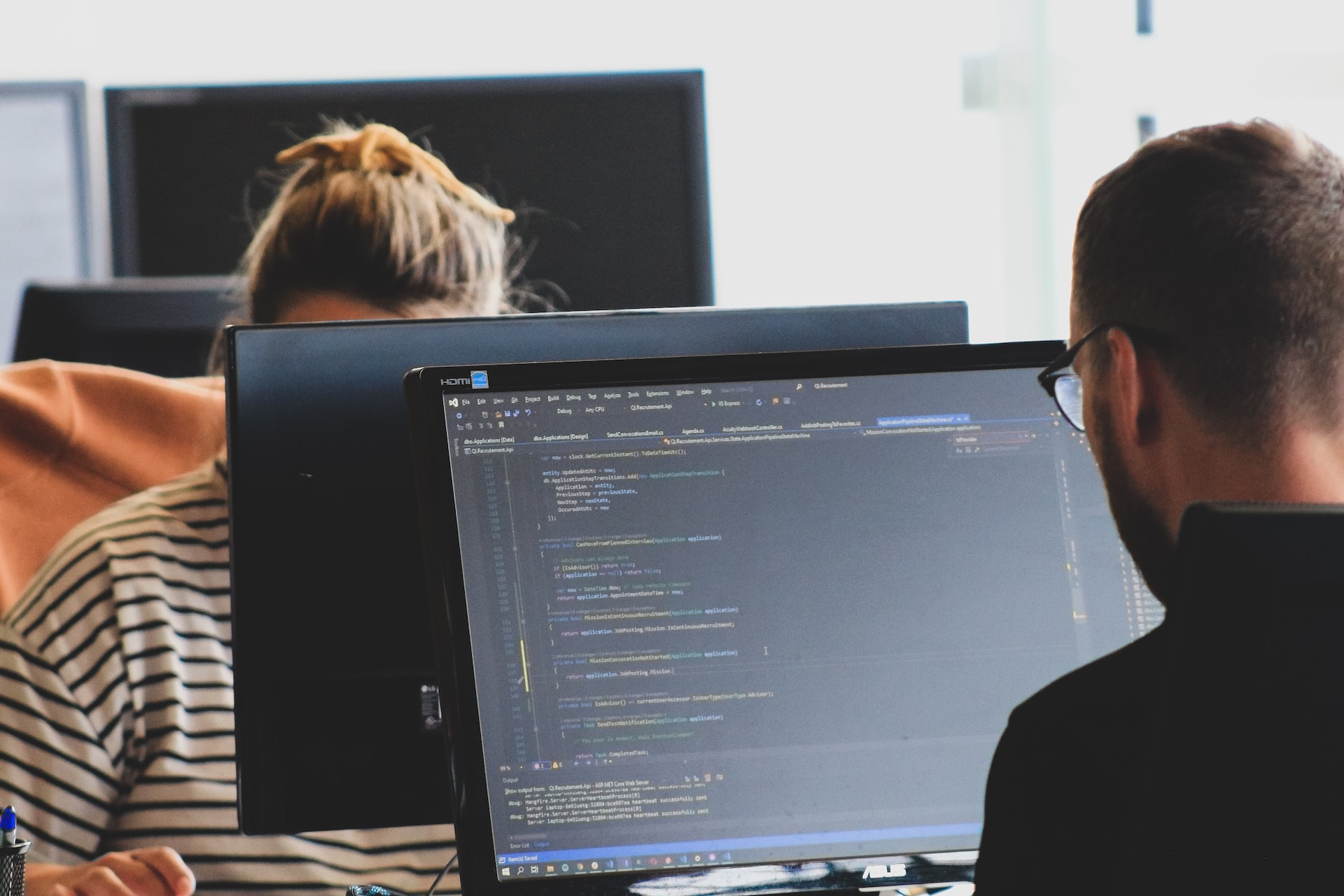 Two people working on computers in an office, utilizing ASP.NET for their tasks.