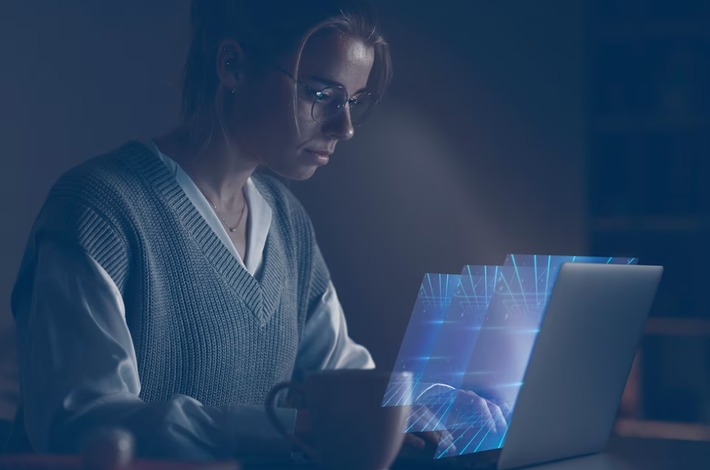 woman in glasses sitting in front of the laptop with three digital screens over it