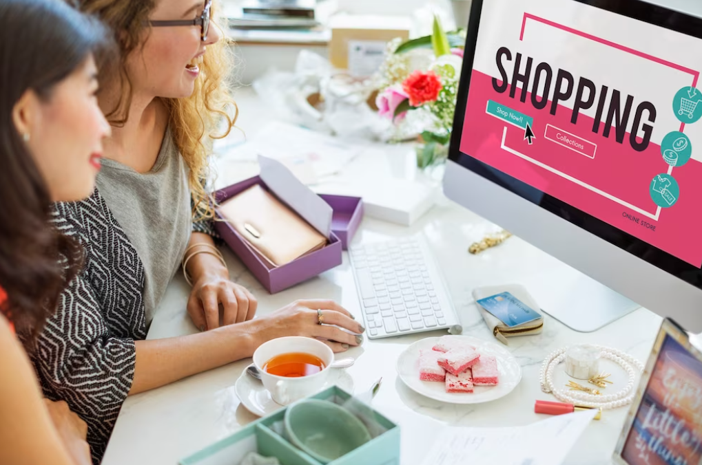 two women sitting at the table in front of a computer screen with a shopping website on it